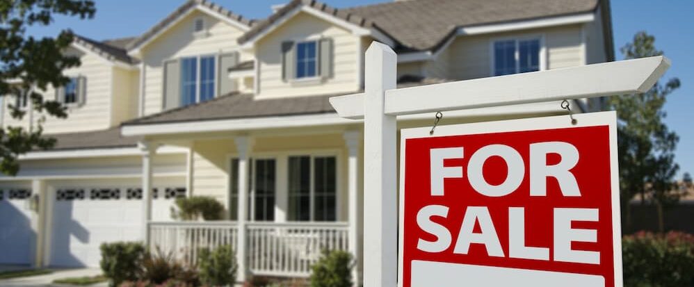 Red and white For Sale sign in front of a suburban home, representing the process of selling a house.