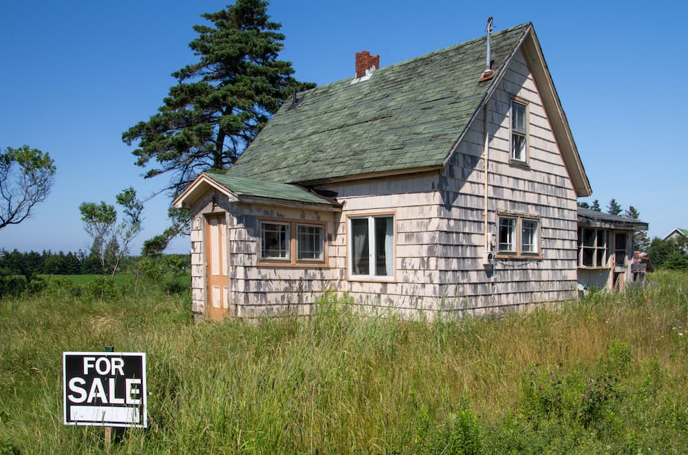 An older weathered house for sale in a rural field, illustrating the process of how to sell a house as-is for cash to an investor.